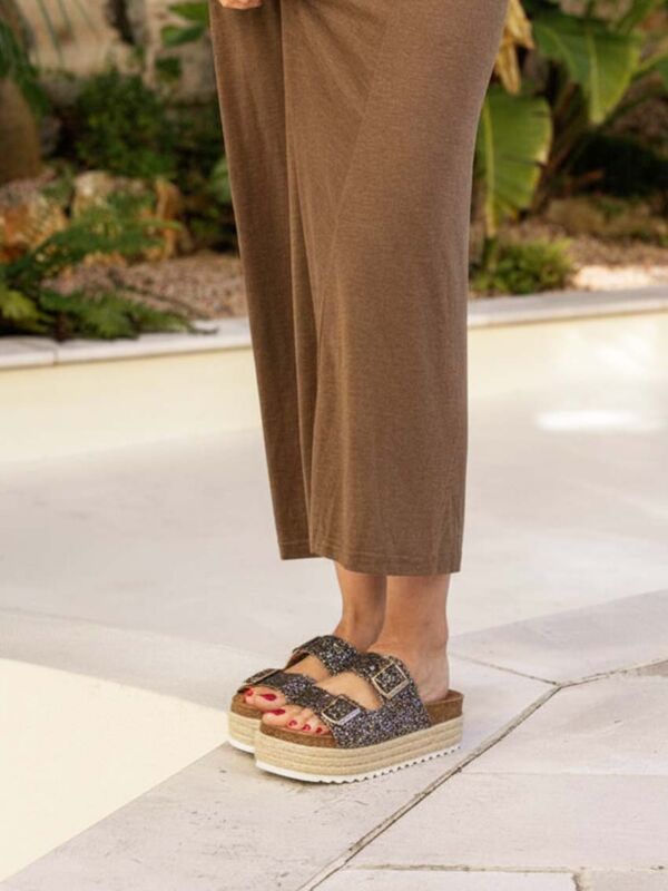 Femme portant des mules Sweet Lemon compensées à paillettes avec double bride à boucles et semelle plateforme effet corde, associées à une robe longue marron