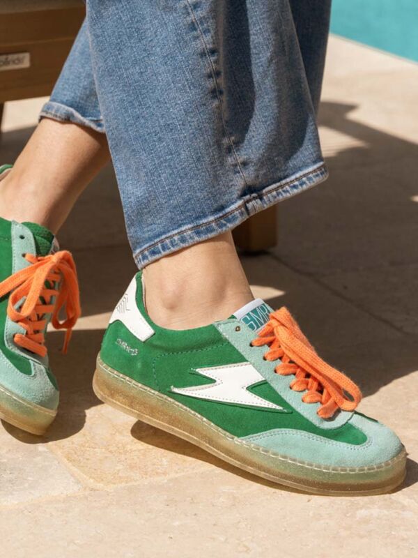 Basket femme originale et tendance Semerdjian SMR23 : modèle vert émeraude et orange vif avec logo éclair blanc, semelle translucide, portée avec un jean décontracté au bord de la piscine.
