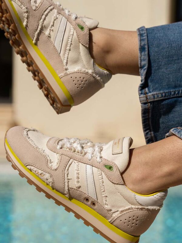 Sneakers Serafini Bella beige et blanche avec détails jaune fluo : baskets raw edge effilochées avec lacets texturés blancs, semelle crantée et finitions brut. Portées avec un jean au bord de la piscine.