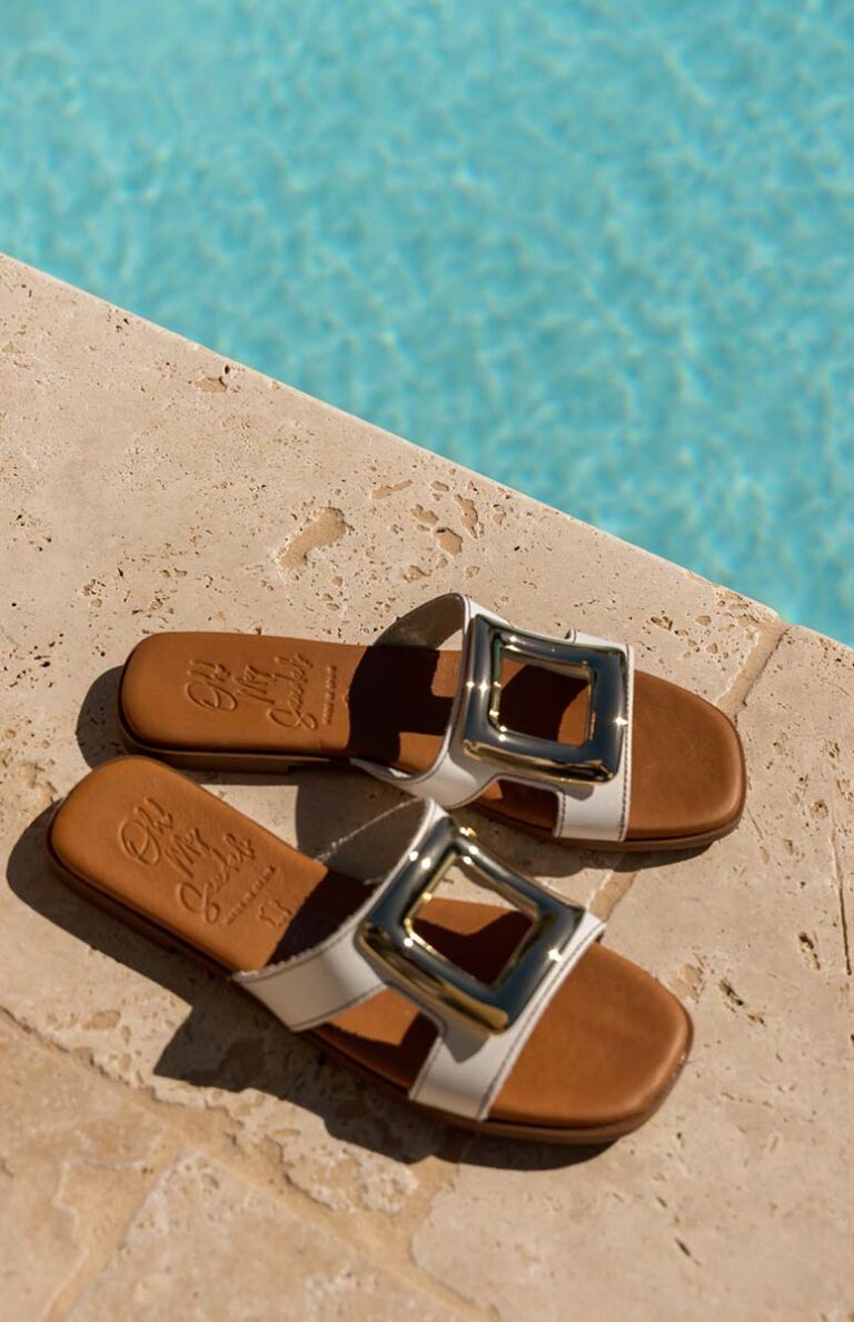 Sandales plates été Oh My Sandals blanches à boucle dorée posées au bord d'une piscine - chaussures plates confortables pour femmes - collection été 2026