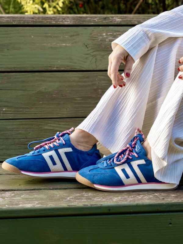 Sneakers femme Back 70 bleues avec bandes blanches, lacets rose et bleu et semelle gomme, portées avec un pantalon clair