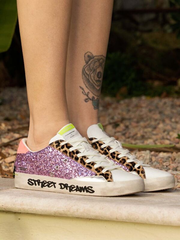 Sneakers femme Crime London blanches avec paillettes roses, détails léopard, lacets blancs et semelle effet vintage, portées en extérieur
