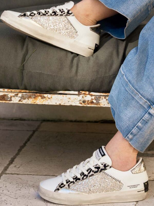 Sneakers femme Crime London blanches avec empiècements pailletés argentés, détails léopard noir et blanc, lacets blancs et semelle effet vintage
