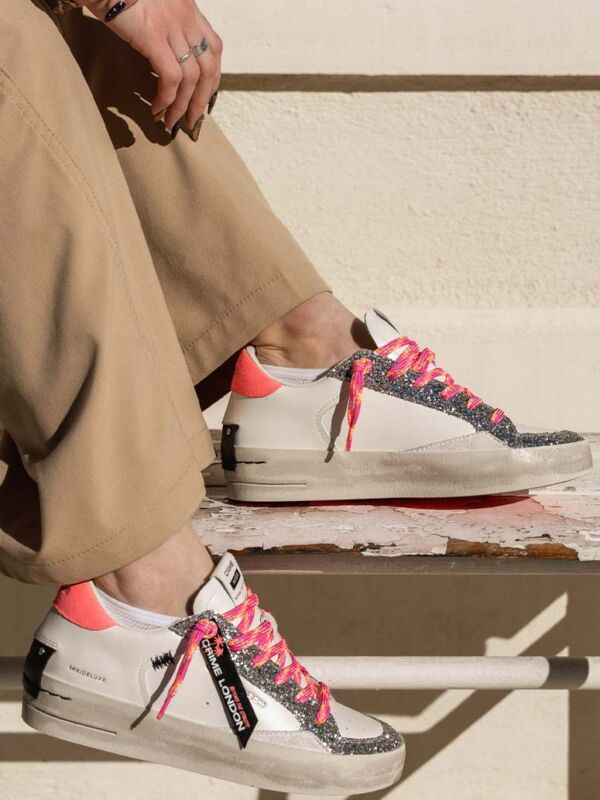 Sneakers femme Crime London blanches avec empiècements pailletés argentés, lacets roses multicolores, détail fluo au talon et semelle effet vintage