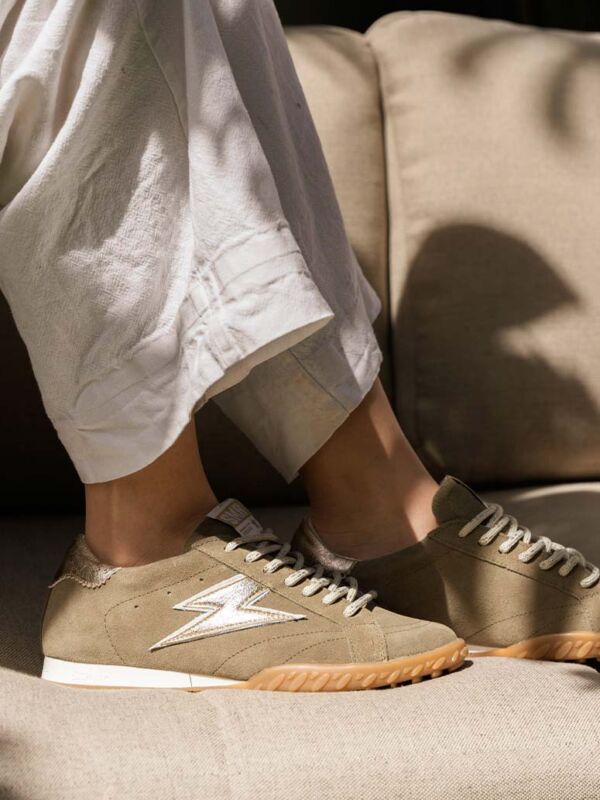 Sneakers Semerdjian Mary kaki et doré : modèle en suède olive avec logo éclair métallisé or, semelle gomme et lacets crème. Portées avec un pantalon lin blanc sur canapé beige.