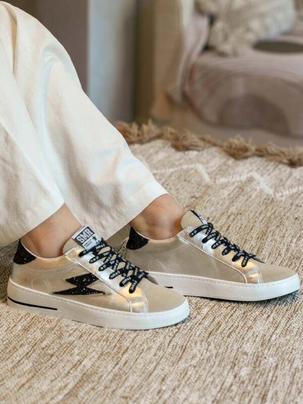 Sneakers femme SMR23 Semerdjian Maya doré avec éclair noir, lacets noirs et semelle blanche, portées en intérieur