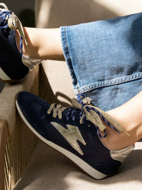 Sneakers Semerdjian June D482 bleu marine avec logo éclair doré métallisé. Baskets rétro en suède et nylon, lacets dorés, portées avec un jean sur canapé.