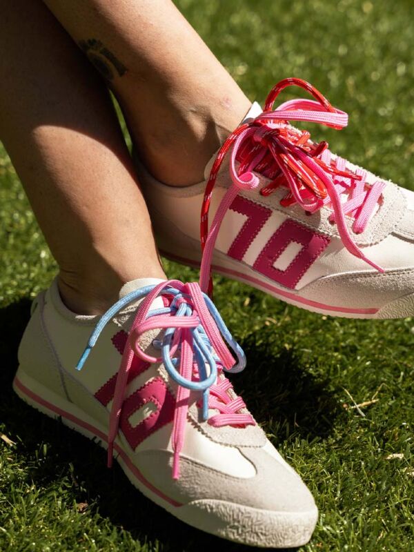 Sneakers Back 70 modèle Leon femme - Baskets blanches avec empiècements rose fuchsia et lacets multicolores bleu et rose, style tennis rétro vintage sur pelouse.