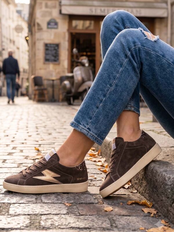 Idée de look moderne avec un jean bleu et une paire de baskets Semerdjian Maya de couleur marron en croûte de cuir, portées dans une rue pavée.