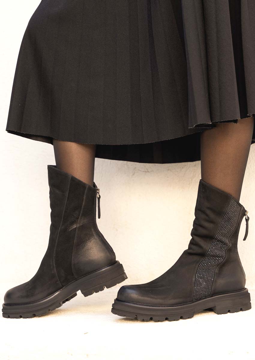 look-bottines-crantees-noires-jupe-longue Femme portant les bottines noires MAT:20 avec une jupe plissée noire et des collants, illustrant un look hivernal tendance et féminin.