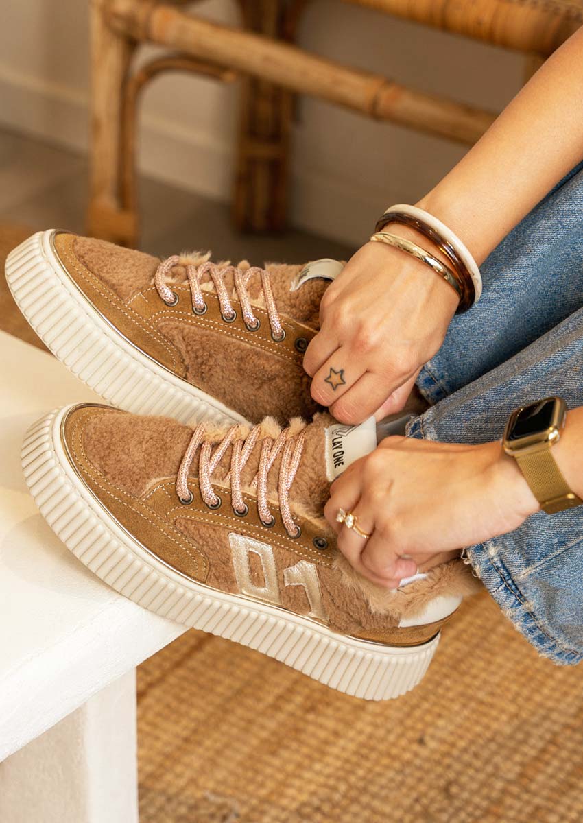 Play One chaussure KOPY 1 Cognac – confort et douceur à enfiler chaque jour Femme enfilant sa Play One chaussure KOPY 1 Cognac : basket femme fourrée synthétique, lacets scintillants rose sable, semelle plateforme blanche, jean bleu
